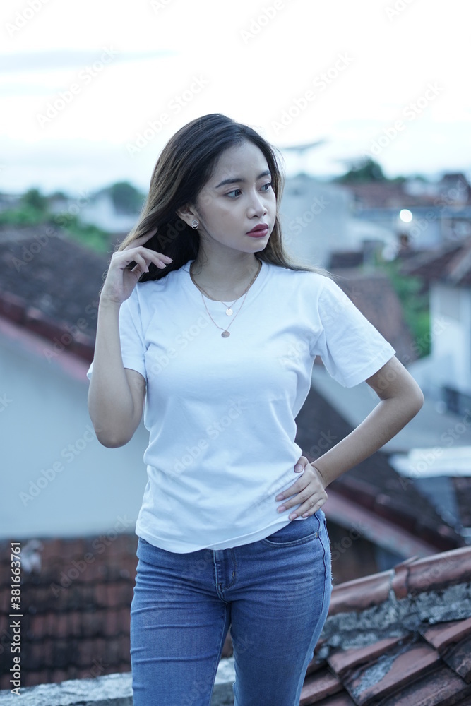 Stylish blonde girl wearing a white shirt on the roof of the building with a view of the clear sky. female t-shirt models for mockups and templates.