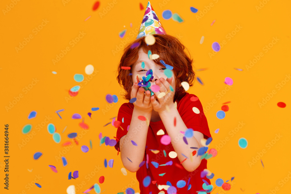 happy birthday! ginger child boy with confetti on yellow background.