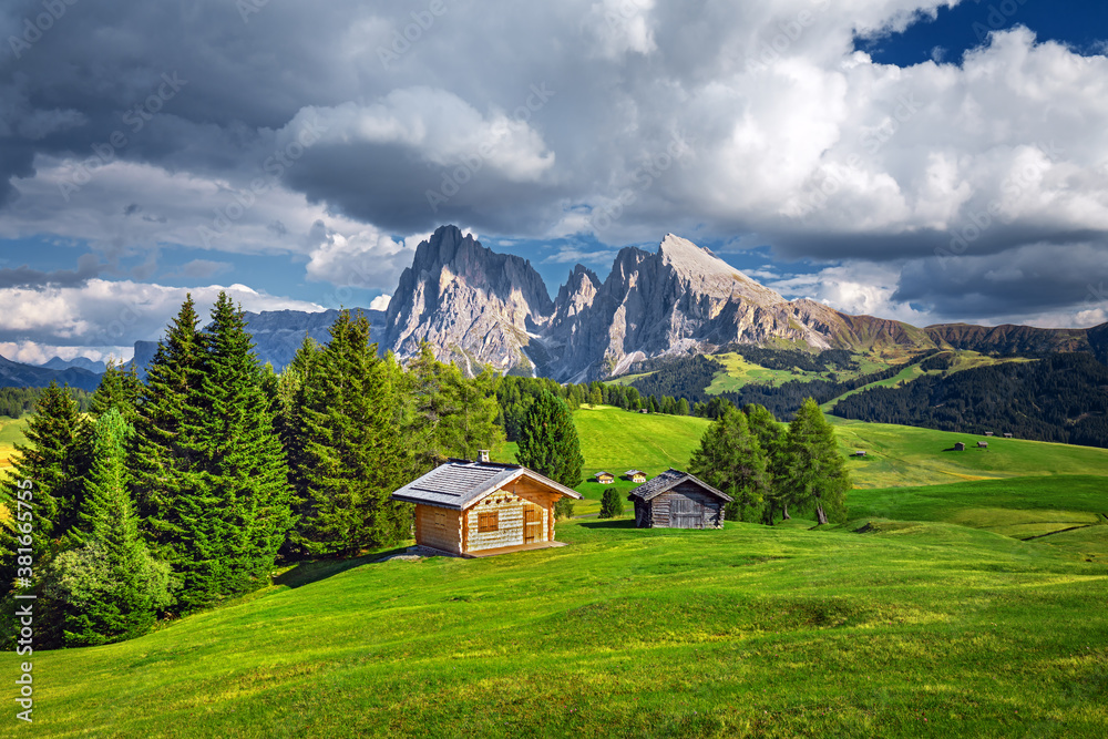 Famous Alpe di Siusi - Seiser Alm with Sassolungo - Langkofel mountain group in background at sunset. Wooden chalets in Dolomites, Trentino Alto Adige region, South Tyrol, Italy