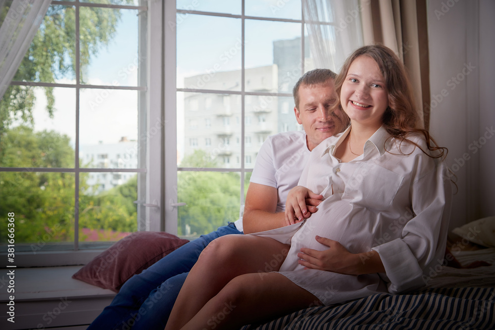 Cute couple including a pregnant woman and a caring man together on the bed on the bed with white linen