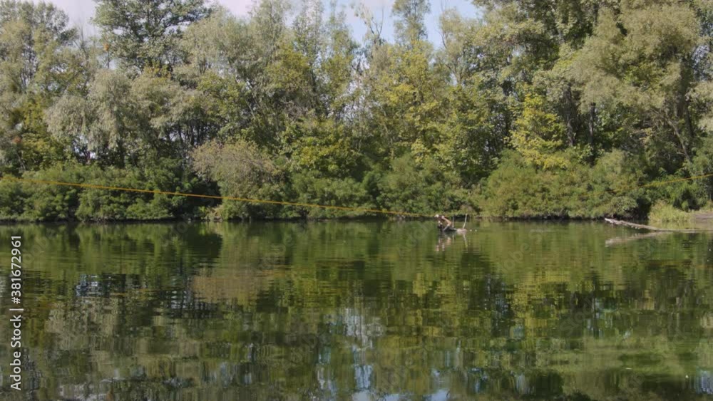 Caucasian man practicing slackline over the surface of the river in the forest. A man practices highlining over water in summer at dawn.