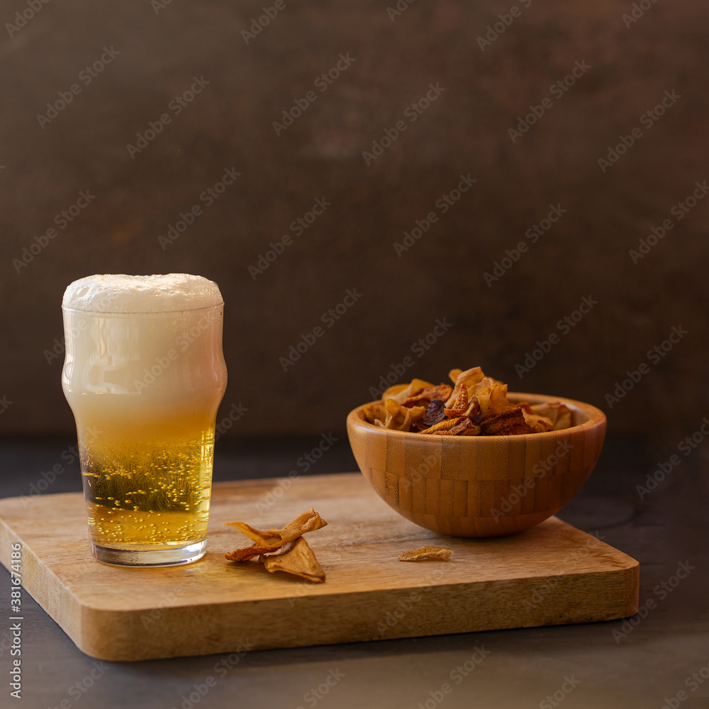 Cold beer in a glass a and bowl of vegetables chips crisps on a wooden try. Cold beer in a glass a and bowl of vegetables chips crisps on a wooden try.