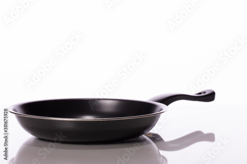 black fry pan, skillet reflected in glass table surface isolated on white background side view. Home cooking concept.
