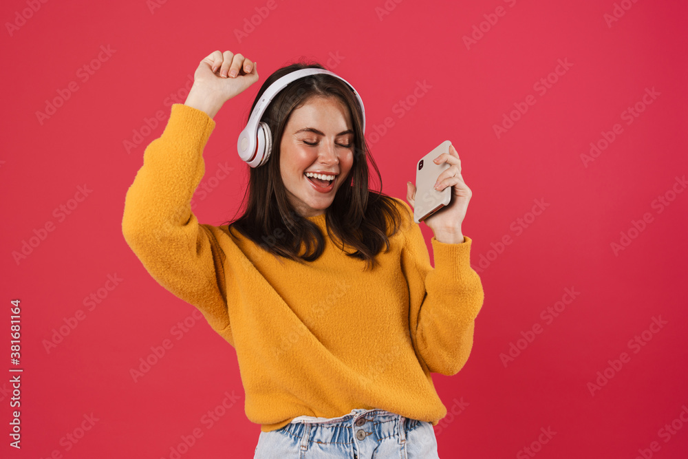 Image of joyful brunette girl in headphone holding cellphone while dancing Image of joyful brunette girl in headphone holding cellphone while dancing