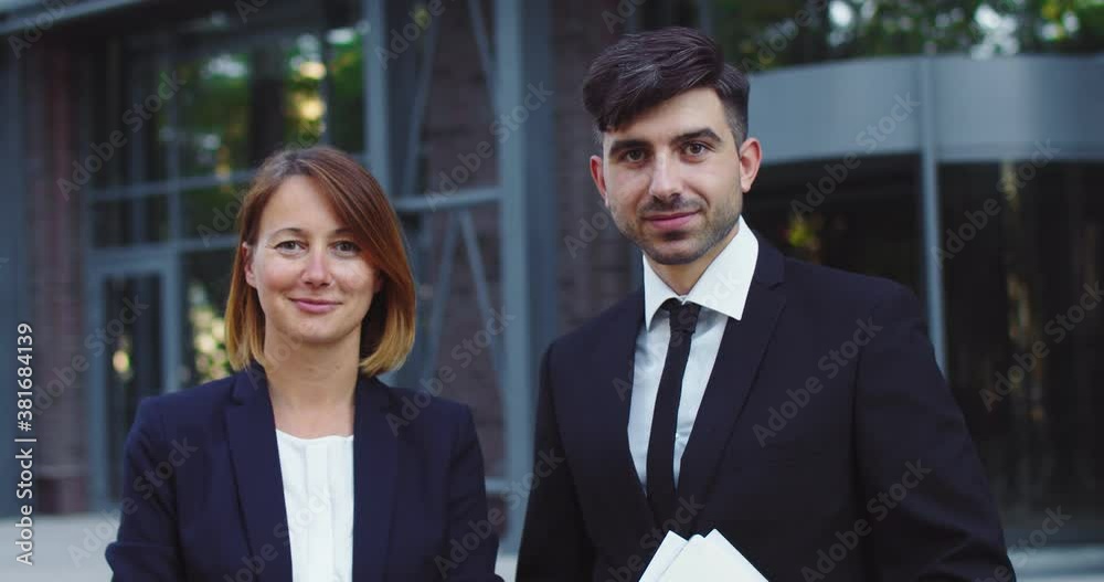 Portrait of male and female corporation collegues outside modern office building in business district. Good-looking man and woman workers in formal suits looking at camera. Profession concept.