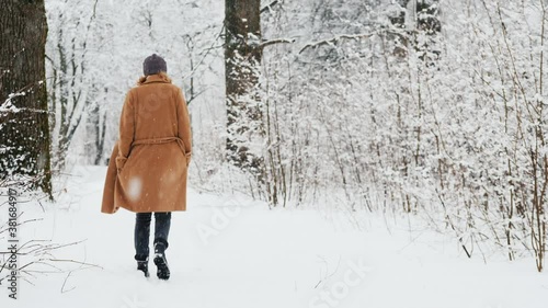 Back view of Stylish middle-aged woman walks in snow park photo