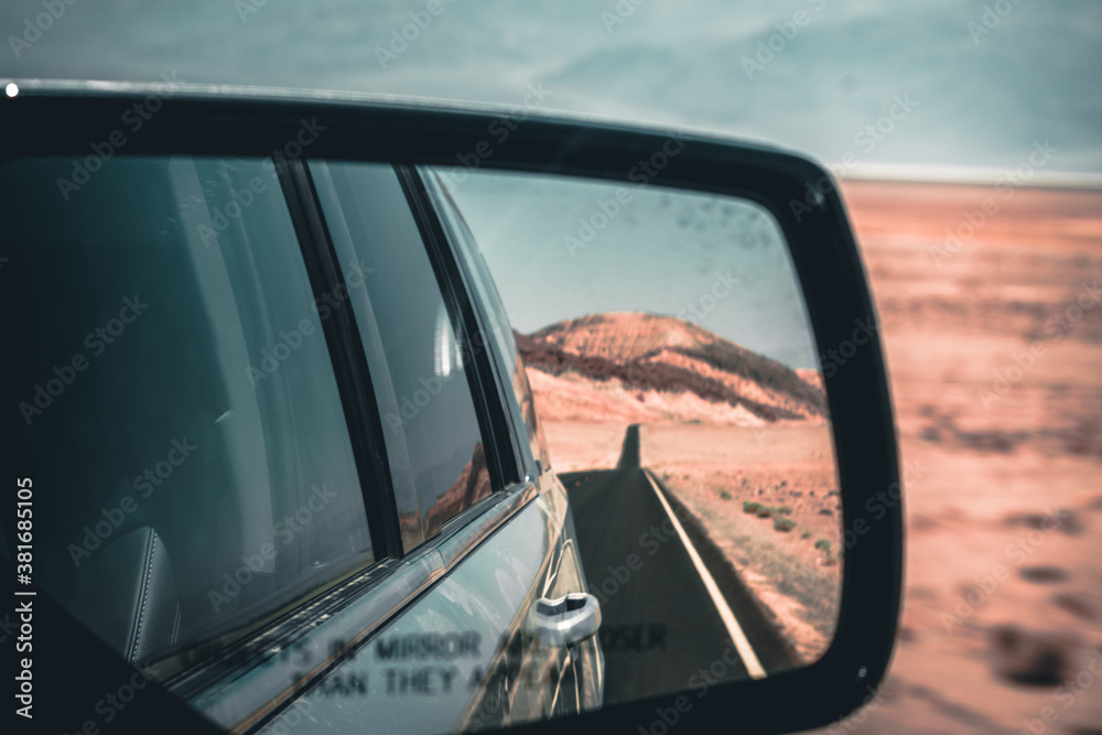 View through the side mirror to the back where a long road leading into nothing in the death valley is visible