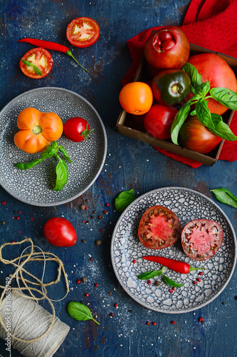 Multi-colored ripe tomatoes and basil leaves on ceramic plates on a dark background, top view. photo