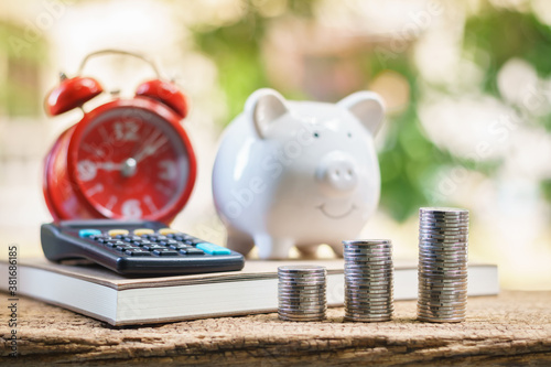 Stack coins with the benefit from dividends and piggy bank alarm clock and calculator put on the account book on the table in the backyard, Saving money for business Investment and spending concept.