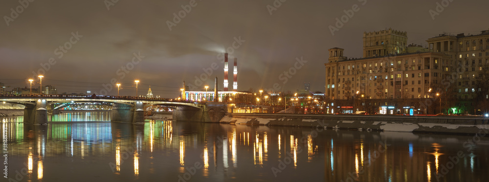 Novoarbatsky bridge and Hotel Ukraine (Radisson Royal Hotel) in bright lights and Moskva river in night winter reflections. Smoking pipes of Heat station.