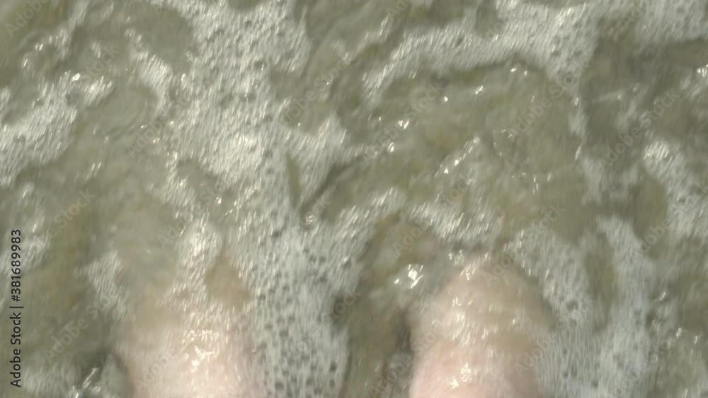 Waves rushing over feet in flip flop sandals on sandy beach in slow motion Waves rushing over feet in flip flop sandals on sandy beach in slow motion