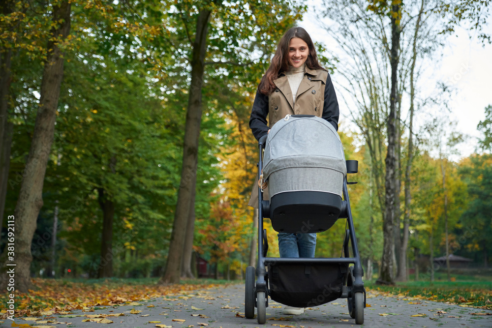 Woman in coat walking with a stroller in the park. Woman in coat walking with a stroller in the park.