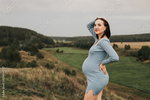 dark-haired pregnant woman of European appearance in a dress on the background of nature. Evening time