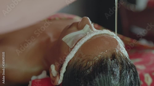 A steady stream of oil flows over the forehead and into the hair of a woman receiving a relaxing Shirodhara treatment during an Ayurvedic retreat. photo
