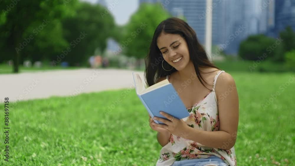 Elegant brunette woman drinking wine and reading a blue book at a lush green park on a beautiful summer day Elegant brunette woman drinking wine and reading a blue book at a lush green park on a beautiful summer day