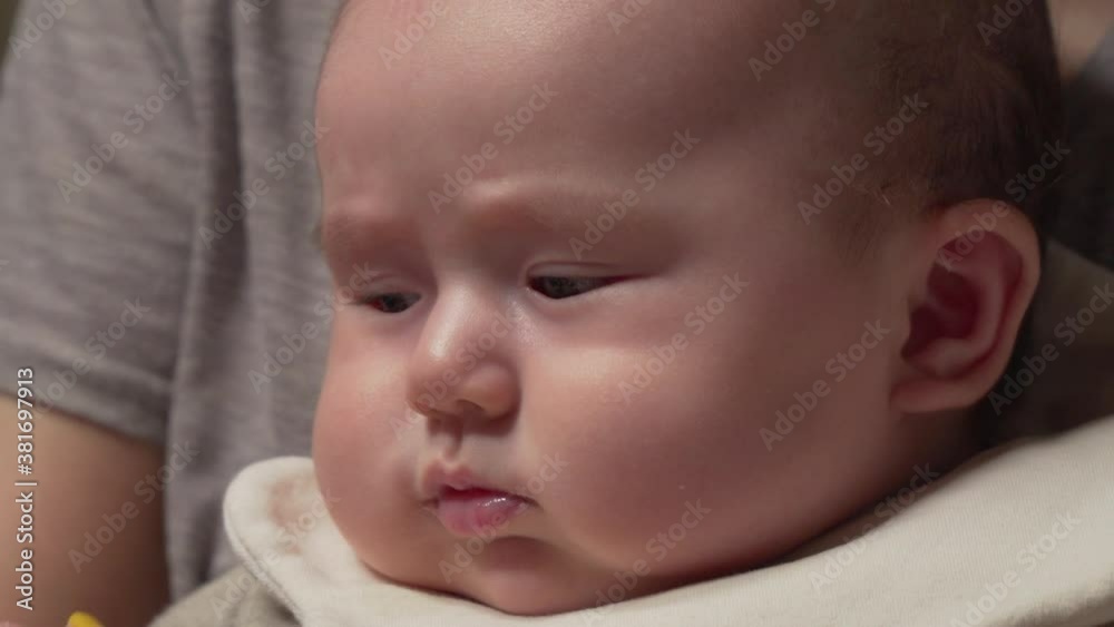 Face Close-up of boring Infant baby sitting on young mother's lap wearing baby bib Face Close-up of boring Infant baby sitting on young mother's lap wearing baby bib