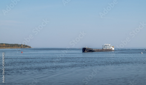 A merchant ship sails in the fairway among the buoys on a large lake or sea. Marine fleet, commercial transportation of goods. Horizontal orientation, selective focus.