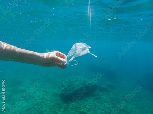 Man collecting a disposable protective face mask thrown in the sea, ocean pollution. Infectious waste from coronavirus