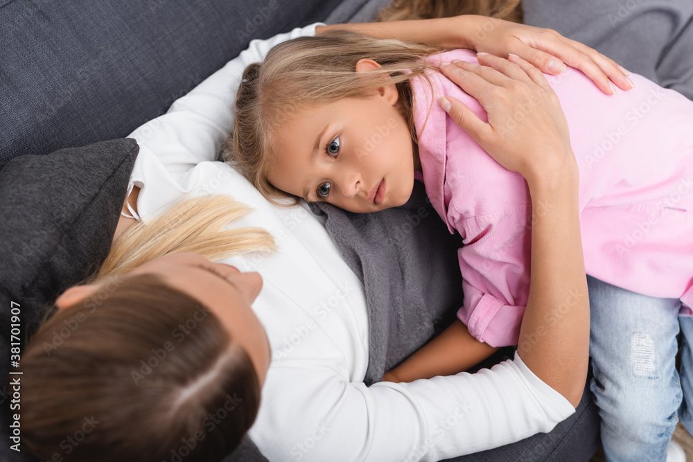 Overhead view of ill woman embracing daughter while lying on couch Overhead view of ill woman embracing daughter while lying on couch