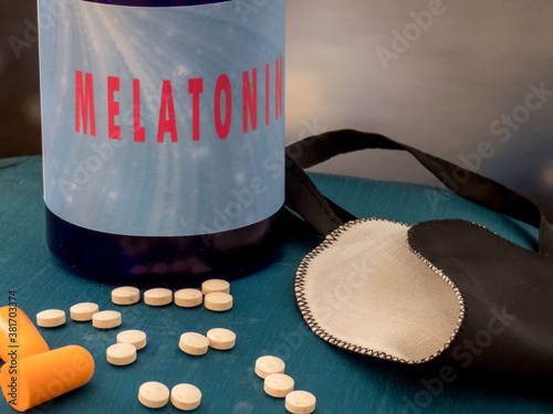 Melatonin supplements, ear plugs and sleep mask for good sleeping on the blue background, close up.