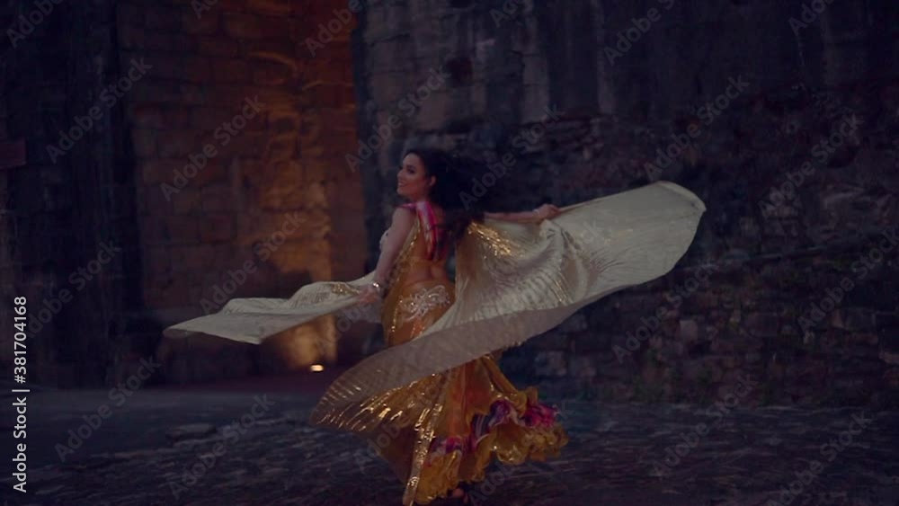 Bailarina de danza del vientre con alas doradas bailando por la noche