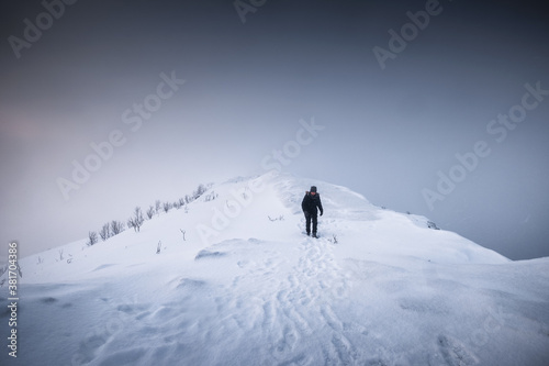 Fotografie Mountaineer man walking on snowy mountain ridge with blizzard in gloomy weather