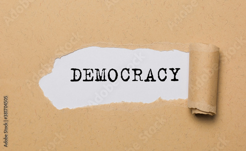 The text Democracy, appearing behind torn paper. The craft paper is ripped. photo