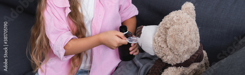 Panoramic crop of kid holding spoon and bottle of syrup near teddy bear