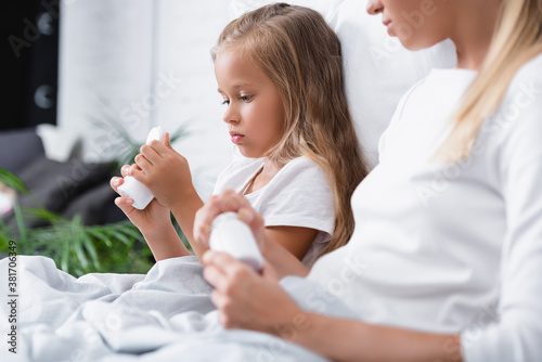 Selective focus of child looking at jar with pills near mother on bed