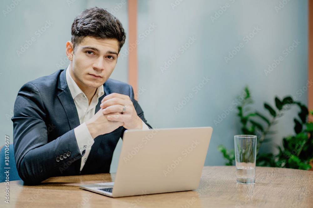 male businessman Manager looking at the camera hands folded in place sitting at a Desk in front of a laptop. new job go to interesting projects male businessman Manager looking at the camera hands folded in place sitting at a Desk in front of a laptop. new job go to interesting projects