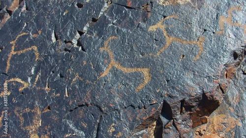 Neolithic ancient carvings (drawing) on black stone. Deer and mountain sheep carvings. Petroglyphs in Central Asia, Uzbekistan Chimgan mountain behind. Slowmo 4 of 26 photo