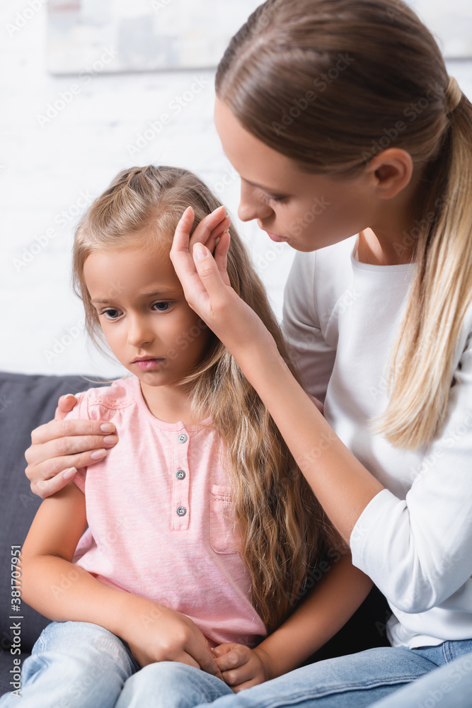 Selective focus of young woman touching forehead of ill daughter at home Selective focus of young woman touching forehead of ill daughter at home