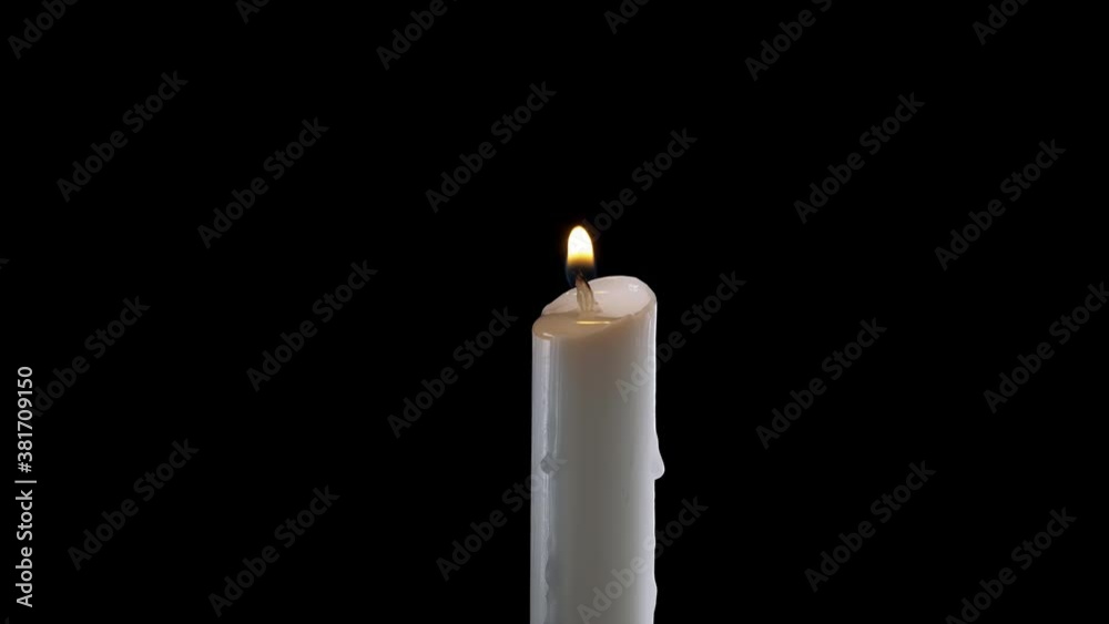 A single white candle burning.Isolated candle burning with dark background.White paraffin candle with yellow shades burns on a black background.Background or illustration of remembrance or celebration
