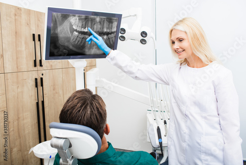 Woman dentist points to an x-ray of the teeth  the patient sits in the dental chair. Installation of fillings  dental treatment