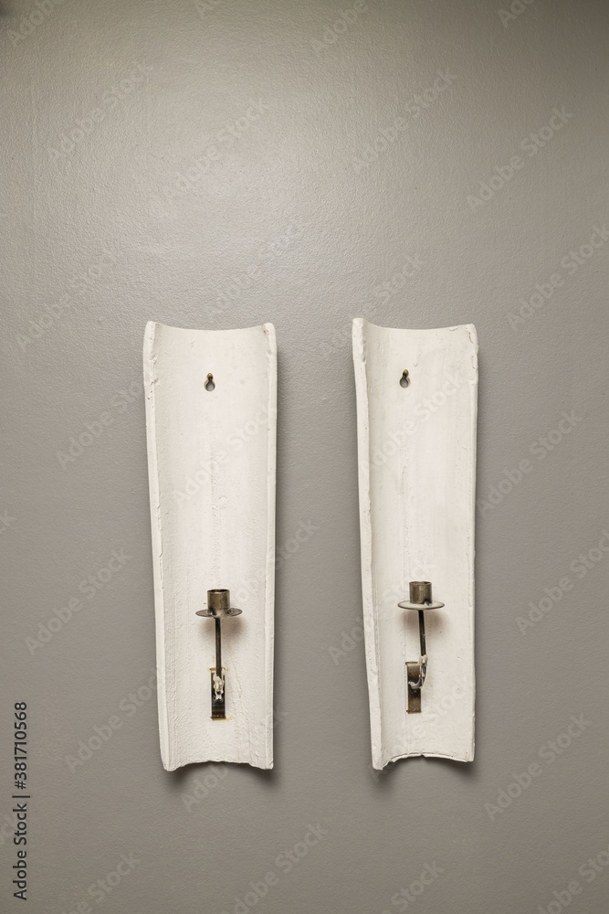 Close up view of two older white candlesticks on grey wall background isolated. Interior decoration details.