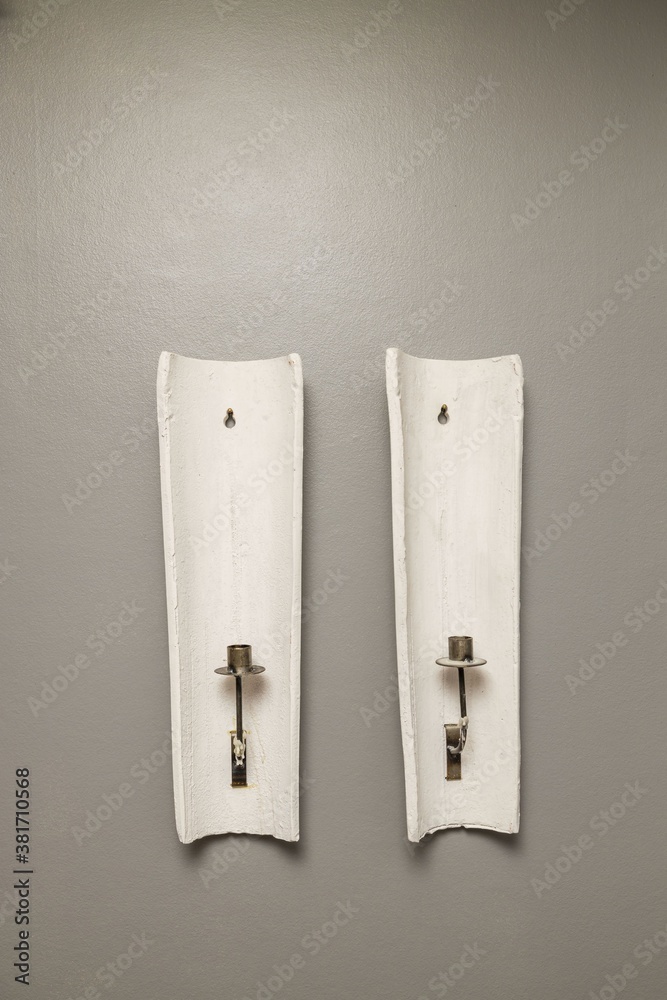 Close up view of two older white candlesticks on grey wall background isolated. Interior decoration details. Close up view of two older white candlesticks on grey wall background isolated. Interior decoration details.