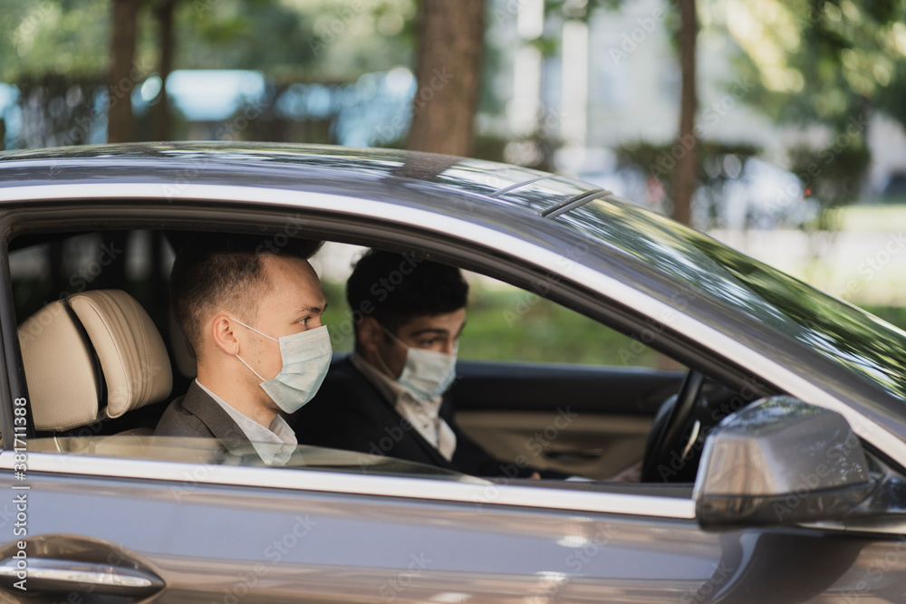 They are sitting in the car wearing protective masks from Covid 19, talking about work, strict business suits. businessmen managers and coronavirus, pandemic, epidemic, infection.