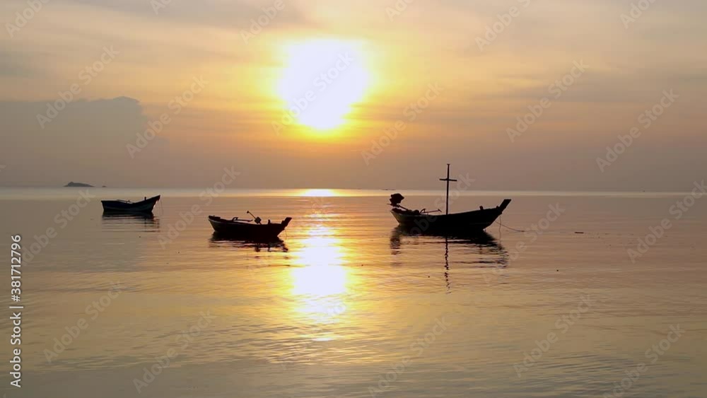 Static evening view of sun setting below the horizon with silhouette of long tail boats parked and floating on the sea during golden hour. Static evening view of sun setting below the horizon with silhouette of long tail boats parked and floating on the sea during golden hour.