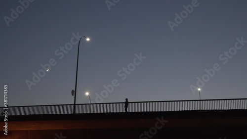 Distant view of several people silhouette slowly walking along the bridge alone at night at moonlight time, low angle wide shot, dramatic cinematic photo