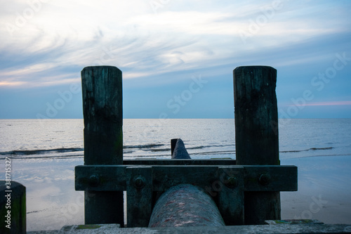 A Pipe With Wooden Poles on Each Side Sticking Out into the Ocean © HRTNT Media