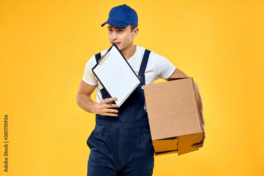 Working man in uniform with box hand delivery loading service yellow background Working man in uniform with box hand delivery loading service yellow background