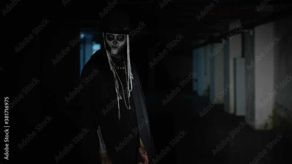 Sinister man with skeleton makeup walking on parking hallway, looking at camera, trying to scare Sinister man with skeleton makeup walking on parking hallway, looking at camera, trying to scare