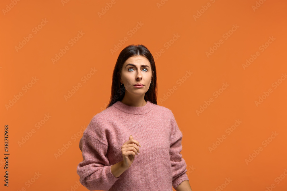 Very unexpected. Photo of surprised woman in pink sweater looks at camera with eyes wide open, smirks face and has puzzled expression, tries to find out something, poses over orange studio wall Very unexpected. Photo of surprised woman in pink sweater looks at camera with eyes wide open, smirks face and has puzzled expression, tries to find out something, poses over orange studio wall