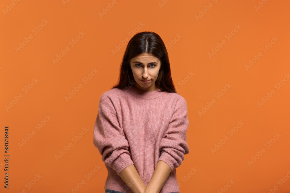 Im really sorry. Portrait of sly cute woman in pink sweater making flirty pose, clasp hands together, looking sullen with apologizes. on orange background