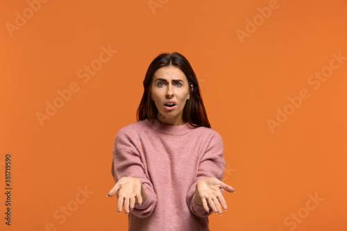 Why. whats next. Portrait of Indignant shocked beautiful woman in pink sweater keeps palm raised, cant understand something, isolated on orange background