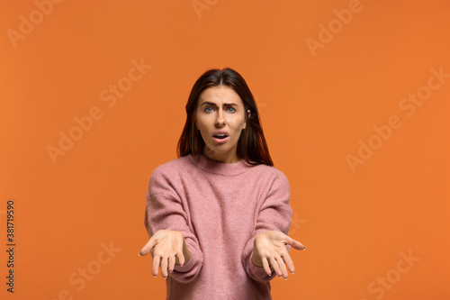 Why. whats next. Portrait of Indignant shocked beautiful woman in pink sweater keeps palm raised, cant understand something, isolated on orange background © 5M