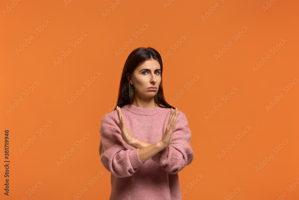 Obraz premium It is forbidden. Portrait of serious woman in pink sweater, makes denial hand gesture, keeps arms crossed over chest, demonstrates stop sign, says no to something or somebody. on orange background