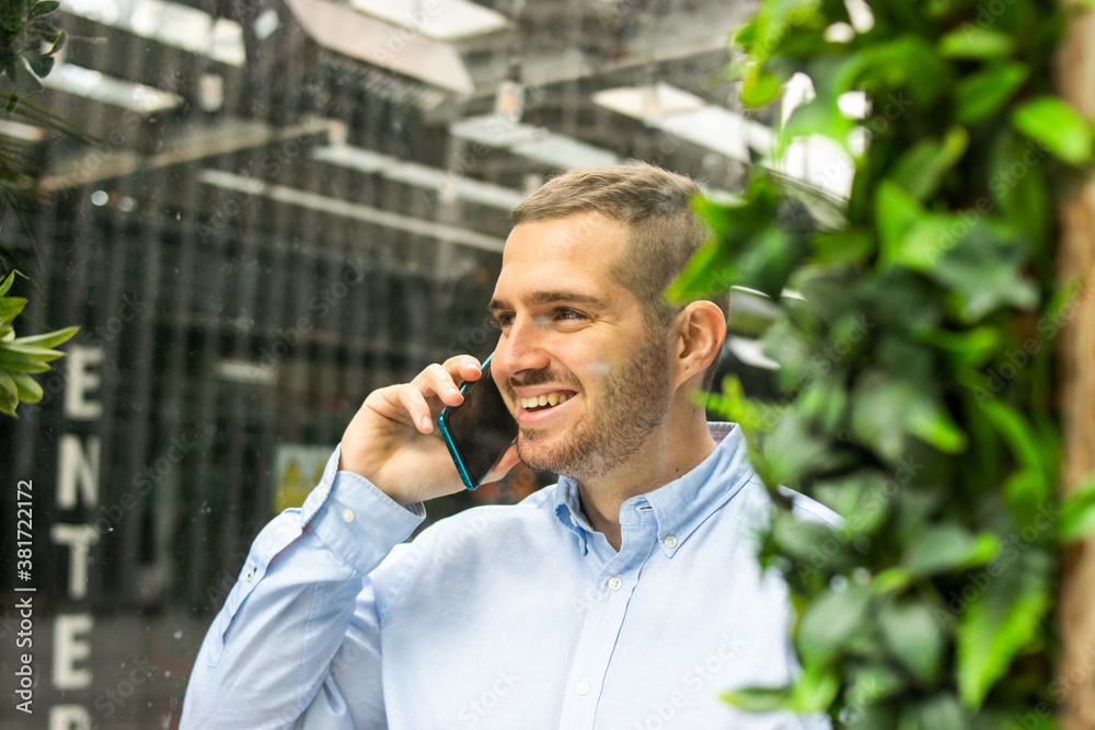 Photo of a young and attractive business man wearing smart casual and elegant clothes talking on the phone while smiling. Smart working. Entrepeneur