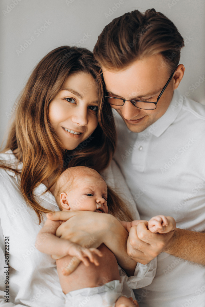 Portrait of parents with newborn baby, loving mom gently hold little daughter in arms, caring dad hold tiny hand of baby girl, smiling, enjoy happy moments, young family concept Portrait of parents with newborn baby, loving mom gently hold little daughter in arms, caring dad hold tiny hand of baby girl, smiling, enjoy happy moments, young family concept