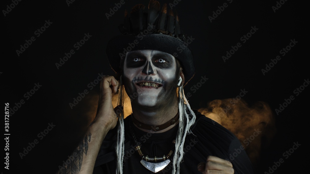 Scary guy in costume of Halloween skeleton wearing earphones, listening music, dancing, celebrating
